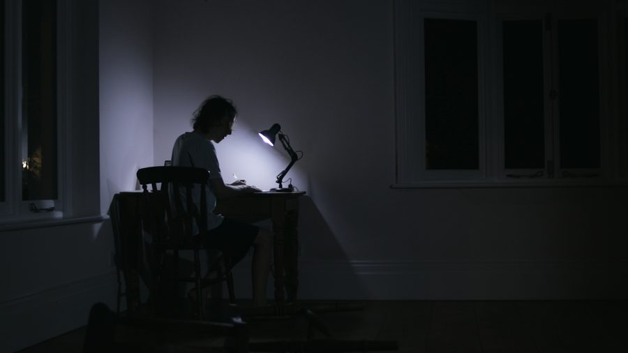 A man works alone at a desk under a single lamp