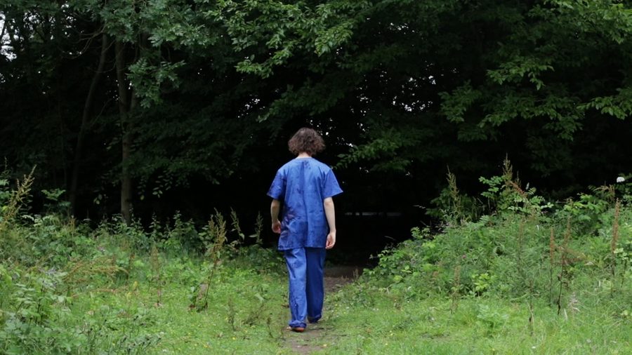 A man in blue scrubs walks away down an overgrown path