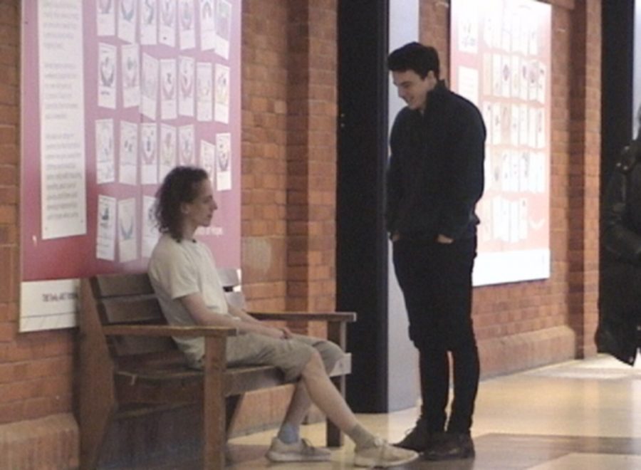 Two young men by a bench in a brick-walled hall