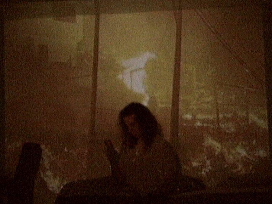 A figure sits in warm, grainy firelight